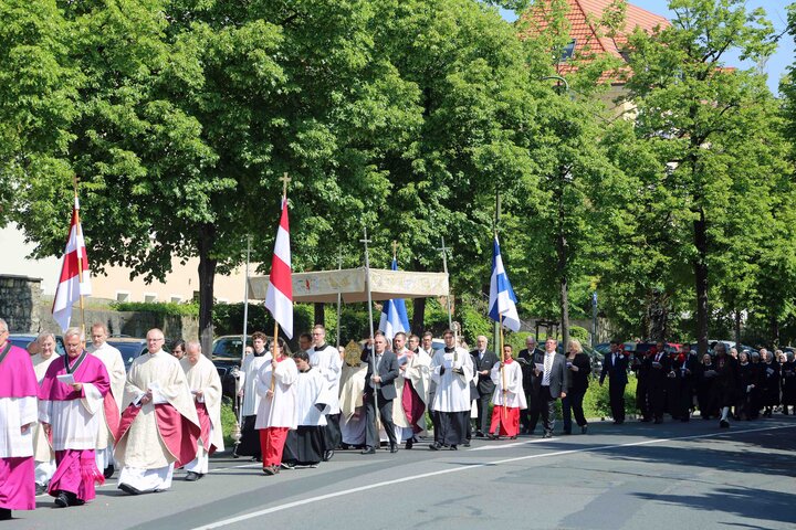 Gläubige ziehen zur Fronleichnamsprozession über eine Straße.