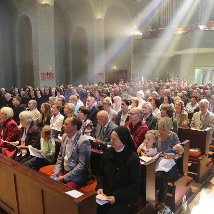 Licht scheint durch ein Kirchenfenster auf Gläubige im Gottesdienst.