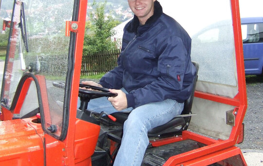 Ein junger Mann sitzt auf einem roten Traktor. 