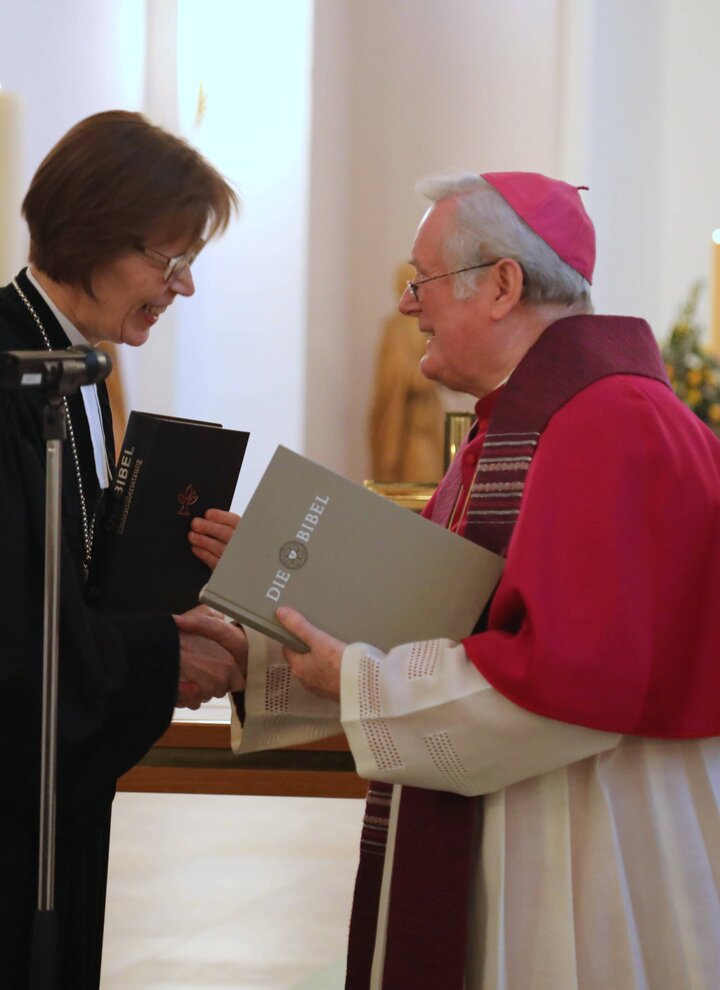 Bischof Friedhelm Hofmann und Regionalbischöfin Gisela Bornowski überreichen sich gegenseitig eine Ausgabe der Einheitsübersetzung beziehungsweise der Lutherbibel.